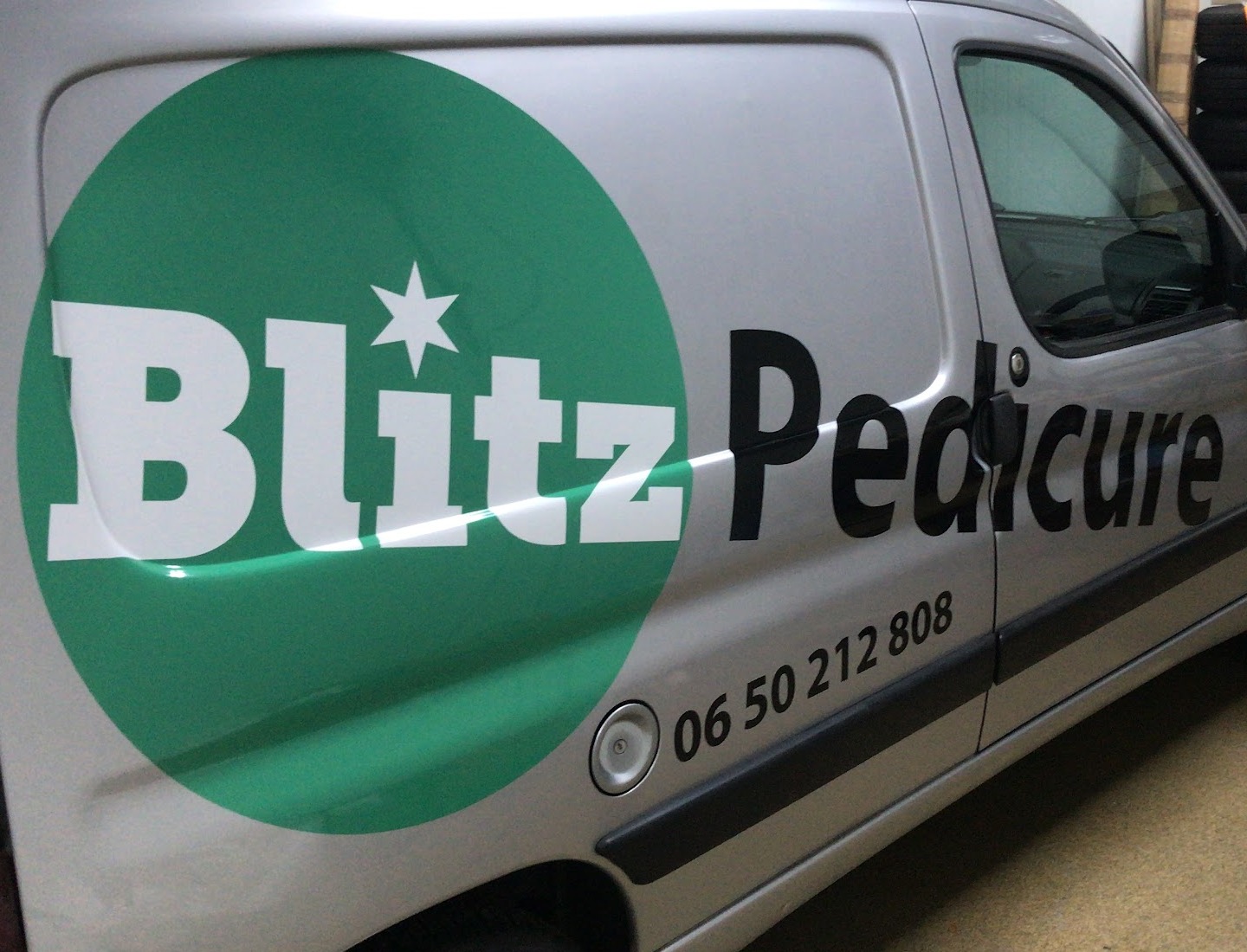 De zilvergrijze Blitz Pedicure bus met het groene logo en het telefoonnummer op de zijkant