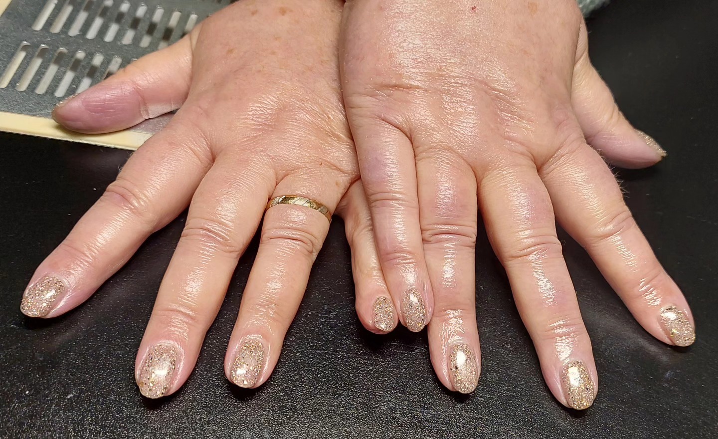 Twee handen met glitternagellak op een donkere tafel